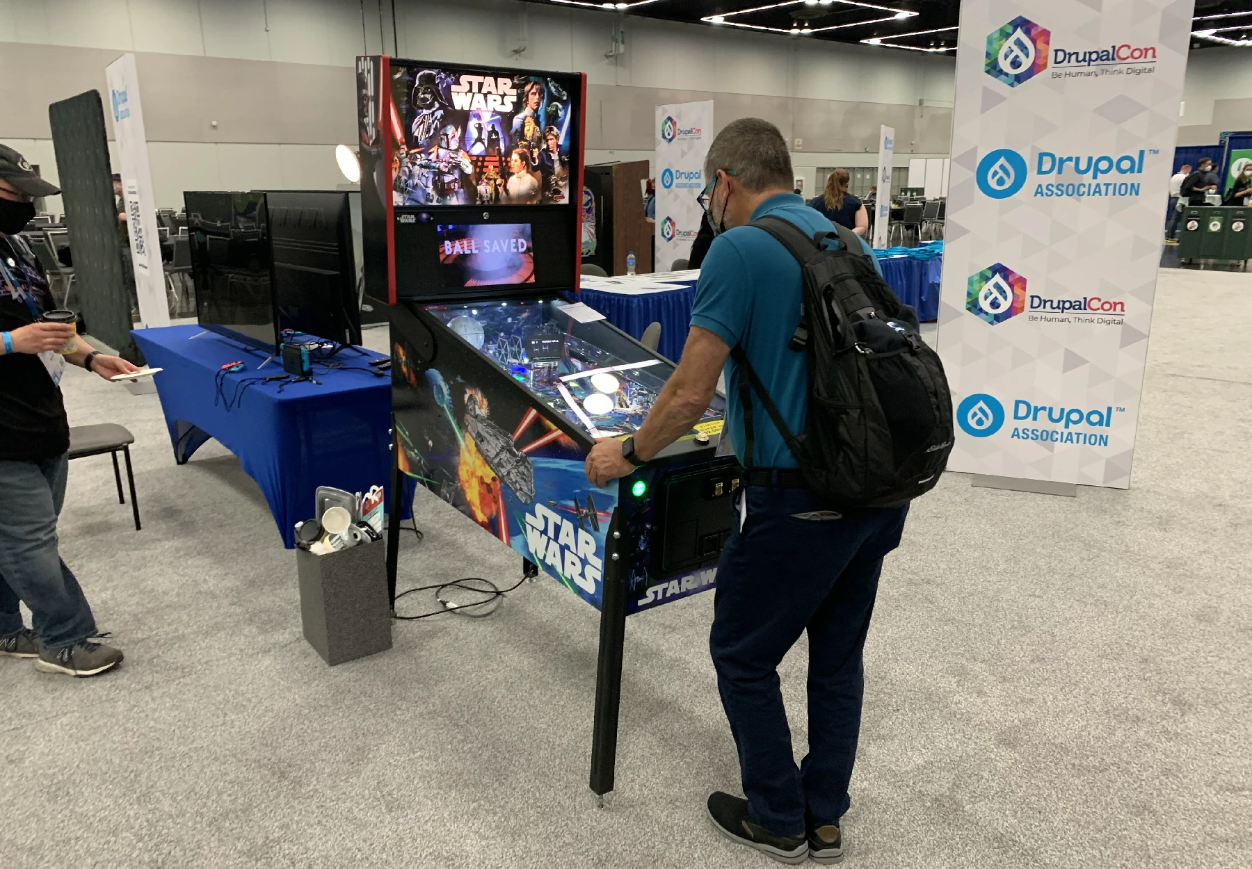 A man standing at a Star Wars pinball machine and playing it furiously