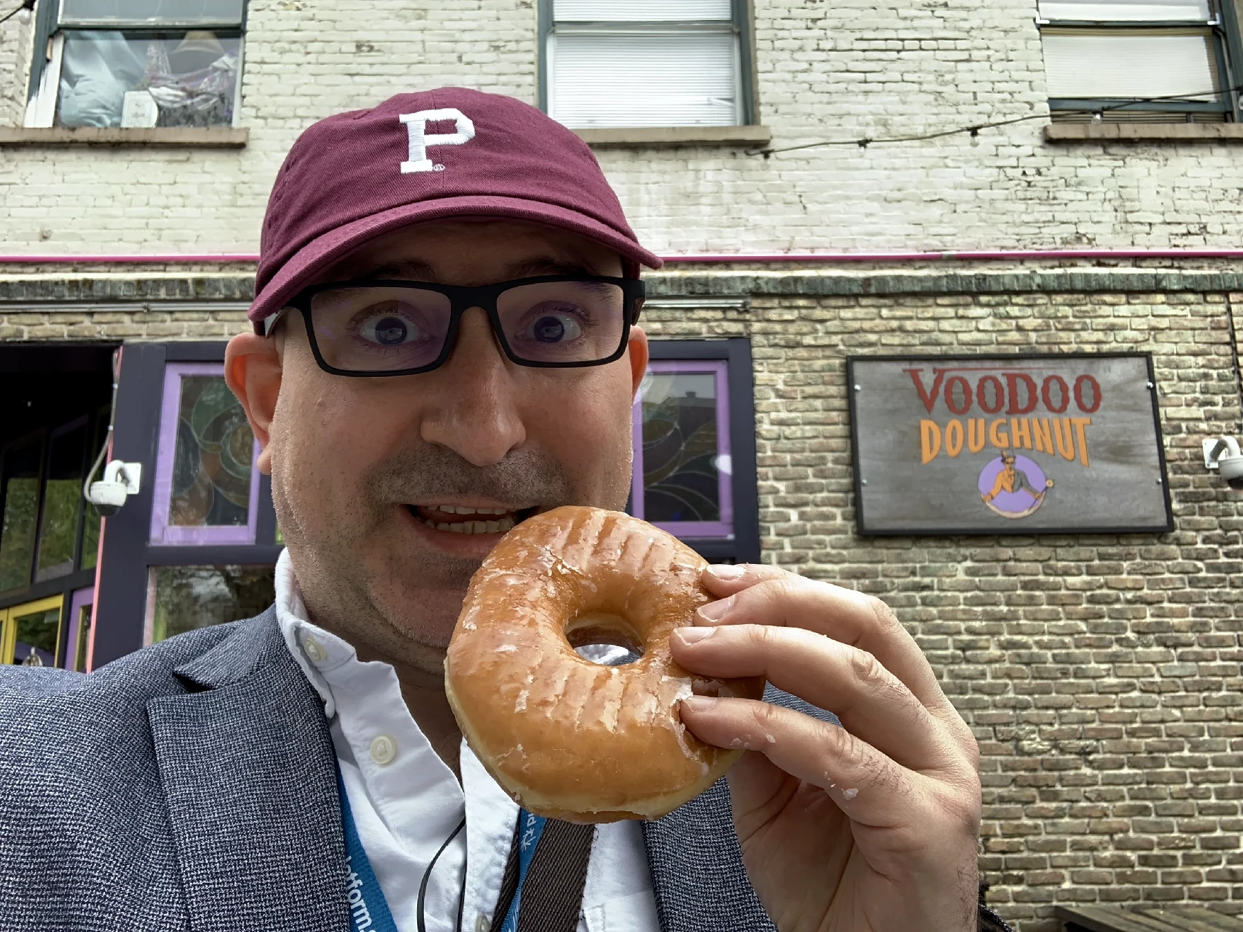 Marin standing in front of Voodoo Doughnut in Portland holding a donut in his hand and looking daftly