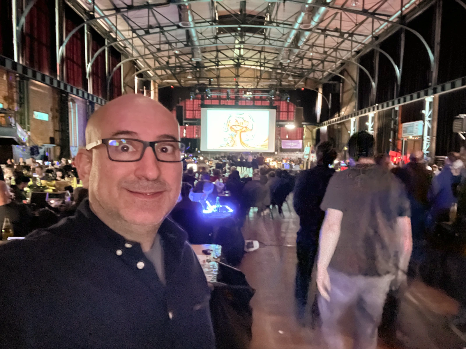 Marin standing in the large hall with his oldskool graphics entry shown on screen at Revision.